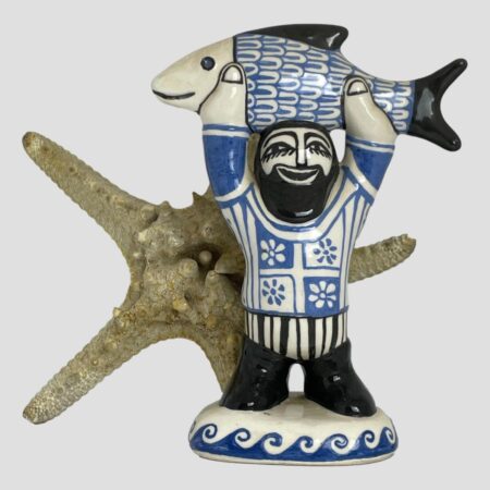 Main photo of fisherman by Bernard Moss seen with a starfish upright and behind for 'sea' effect. The fisherman is holding a large fish raised above his head with both arms up stretched. The whole studio art piece is in just 3 colours; black-hair, facial features, boots, fish tail and fin and face, blue-fish scales, decorations on jumper and waves and cream for everything else. This is such a smile inducing happy piece of studio pottery that anyone will love.