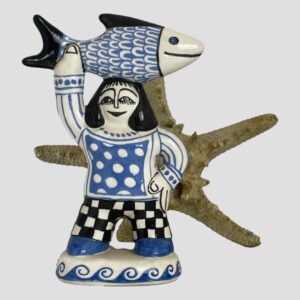 Main photo of Bernard Moss fisherwoman figurine displayed forward facing with a starfish standing upright behind her for effect! Unlike her male counterpart, the fisherwoman is holding her substantial catch aloft by the tail end with just one up stretched arm. The belly of the fish is resting on her head. Her other hand is on her hip. As per her husband, the fisherwoman colourway is cream, blue and black.