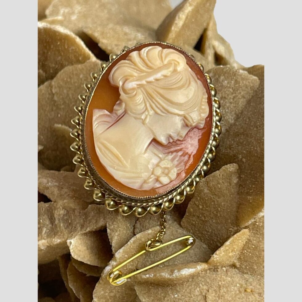 A close up photo of the brooch front this time slightly angled to the right making the lady in profile look as though she is looking deeper downward. The pin of the safety chain is protruding from below the brooch.