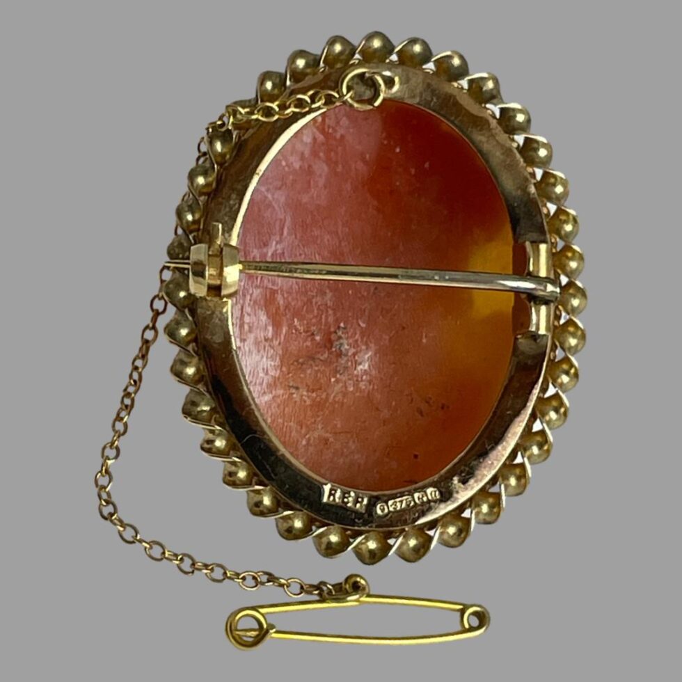 Photo of back of pendant shown upright with pin closed. The safety chain extends from the top of brooch and down left hand side in this picture and the pin is in the centre foreground. The full hallmark is visible at the bottom rim of the brooch.
