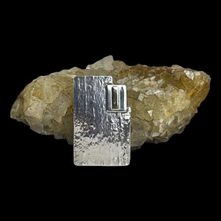 Main photo of Modernist style silver brooch displayed leaning against a rock of natural river quartz with the brooch front forward facing. The cut away area is to the top right corner. The brooch is shown lengthways standing but of course can be worn any way up.