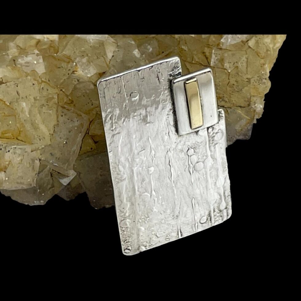 Close up photo of Modernist style silver brooch with the brooch front facing towards the bottom right corner of photo.