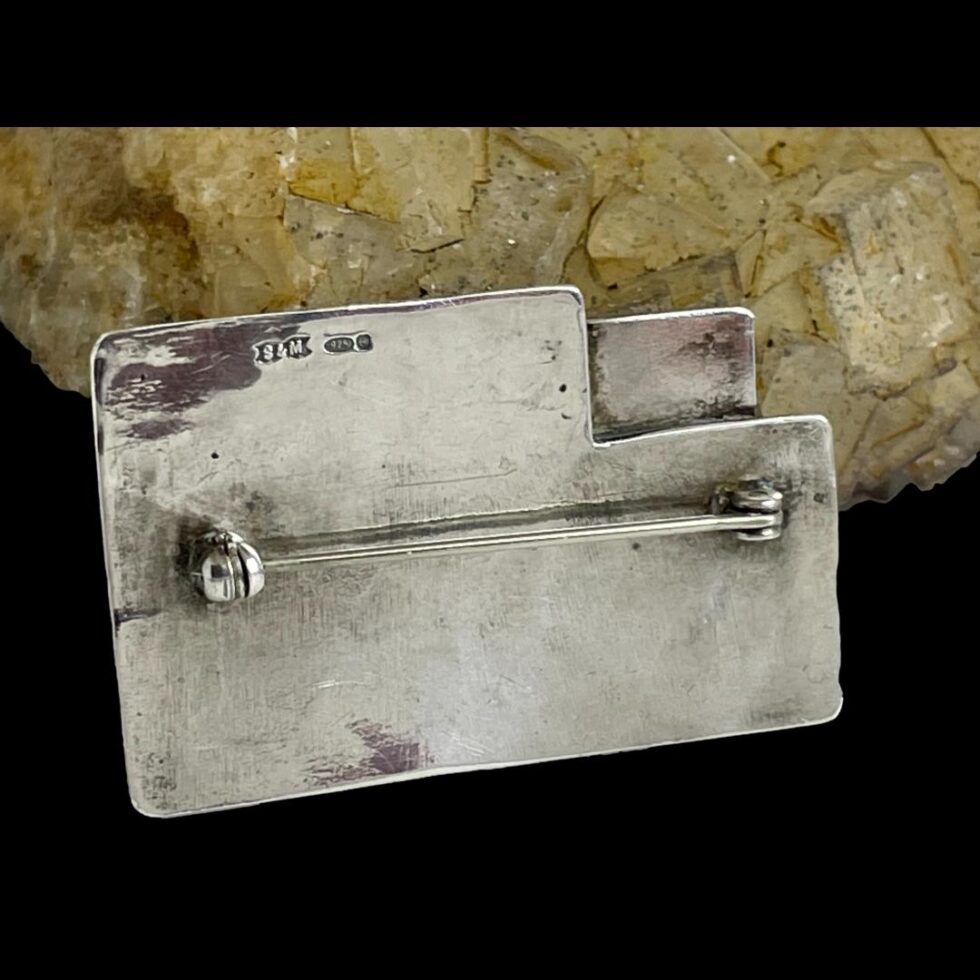 Photo of the back of Modernist style silver brooch shown horizontally long with the cut away area in the top right corner. The hallmark is visible to the left corner of cut away corner.