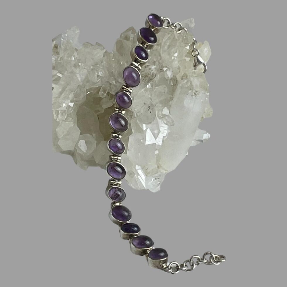 Main photo of sterling silver amethyst brooch displayed laid across a rock of natural quartz crystal and shown vertically. The amethyst cabochons are mixed in colour from lilac to a deeper purple.