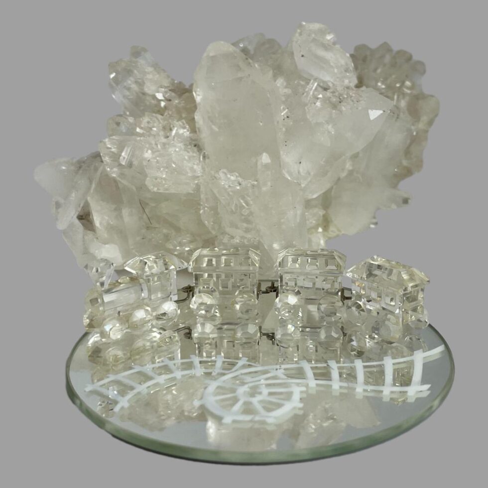 The Swarovski crystal train set displayed on the round mirror track with a lump of natural quartz crystal behind the train.