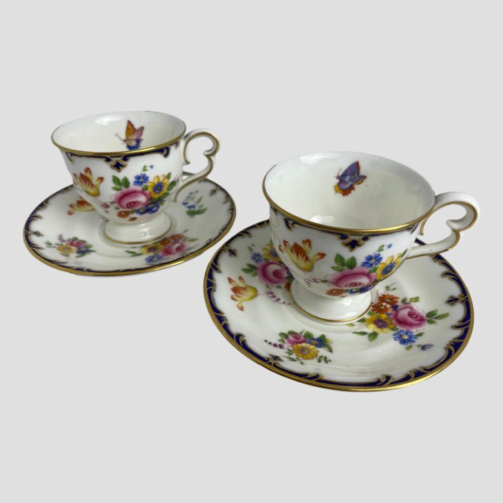 Photo of Cauldon cups and saucers displayed side by side and seen from a slightly raised angle to show the butterfly to inside rim of the cups. The butterflies are different colours .