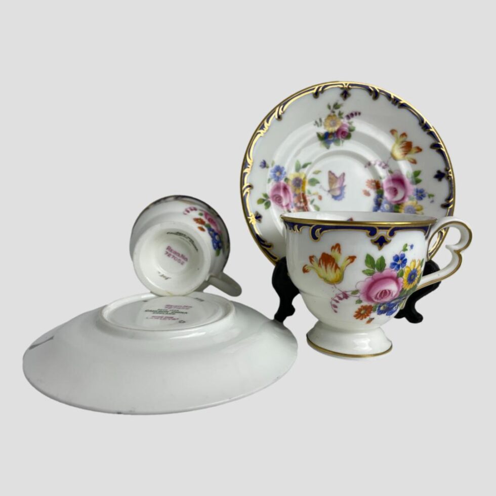 Photo of Cauldon cups and saucers this time displayed with one saucer (right) displayed on a wooden stand and cup posed in front of it and cup and saucer on left displaying the Cauldon stamp on their base.