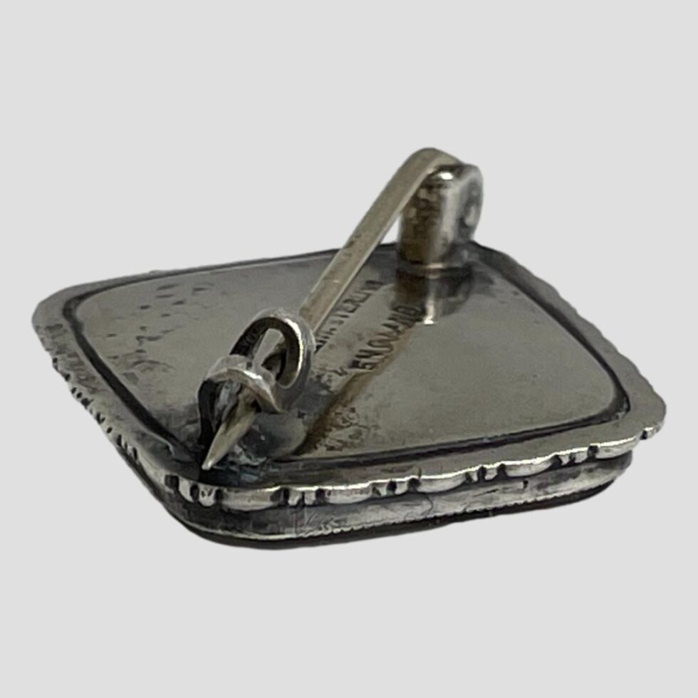 Photo of brooch displayed face down on a flat surface with the pin clasp end in the foreground