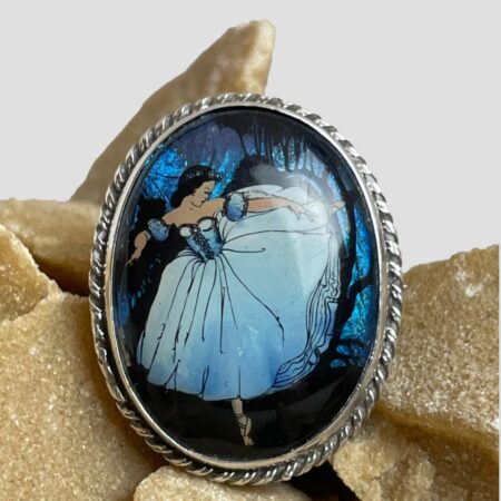 Main photo of Ballerina butterfly wing brooch displayed on top of a rock of natural desert sand rose and shown with the brooch front forward facing. The ballerina is painted in an arabesque pose and appears to be running away with the woods in the background. The woods, in electric blue, are all butterfly wings even the dark shadows of the trees. We are thinking Snow White.