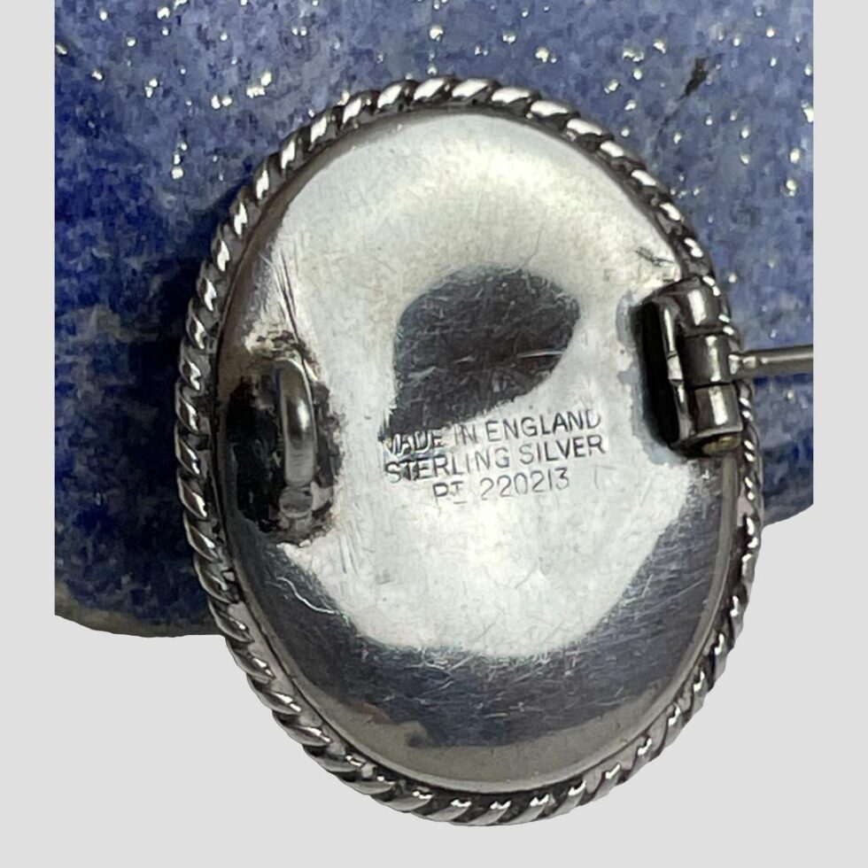 Photo of brooch leaning against a rock of lapis and seen with the back on display showing Made in England Sterling Silver and Pt 220213 (patent number)