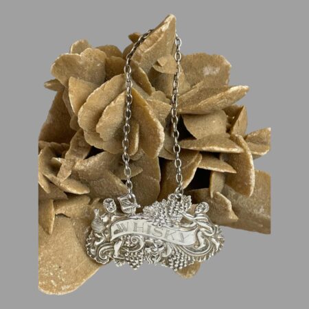 Main photo of silver whisky decanter label displayed hanging from a rock of natural desert rose from its chain. The main part of the label is below with detailed description to follow in next image.