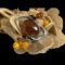 Main photo of sterling silver amber brooch displayed on top of a rock of natural desert sand rose. The central amber is a generously sized oval shape with the silver calla lily flower stems extending out from one side and the flower head leaning over the top of the large amber to finish on the opposite side where the stamen balls protrude. There is no top and bottom to this brooch so it can be worn any way round. The large central amber is a cognac colour with the stamen balls in cognac, butterscotch and honey colours. There is something quite space age looking about this lovely brooch and will definitely attract compliments! In this photo, the brooch is angled so the large oval amber is seen diagonally laid and the balls are positioned bottom left and top right corners.
