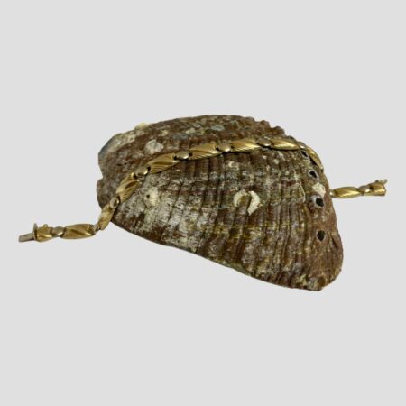 Main photo of 18Kt Egyptian gold bracelet displayed horizontally across the back of a sea shell. The bracelet is made up of rectangular panels with a disc area separating each segment. The gold discs give the bracelet flexibility and neatly slot into an area between panels. The rectangles have curved outer edges and decorated with diagonal lines to each.