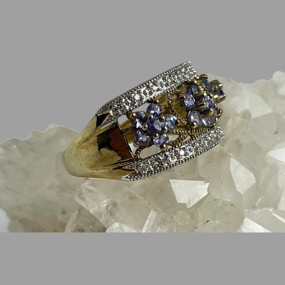 Photo of modern gold tanzanite ring displayed on a rock of quartz crystal with the ring front facing to the right. Nice thick frontage ring for anyone liking a wider ring.