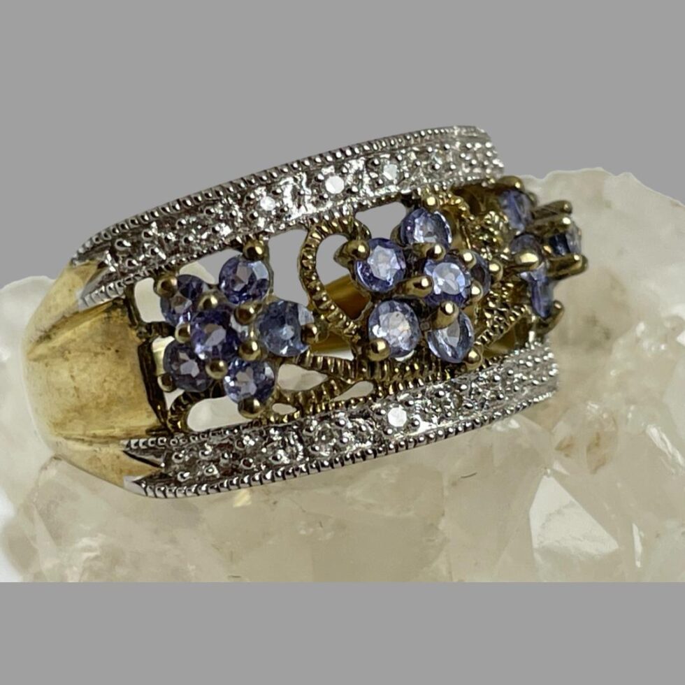 Close up photo of the modern gold tanzanite ring with ring front facing right. The light is catching the tanzanite stones and diamond chips and the ring is full of sparkle.