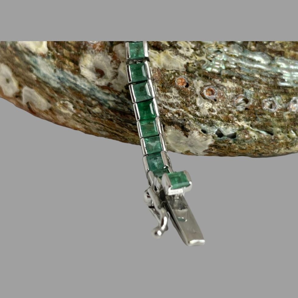 Close up photo of the clasp end with the release button and loop hook safety catch. The release button also has an emerald to it and is raised slightly higher than the rest of the emeralds.