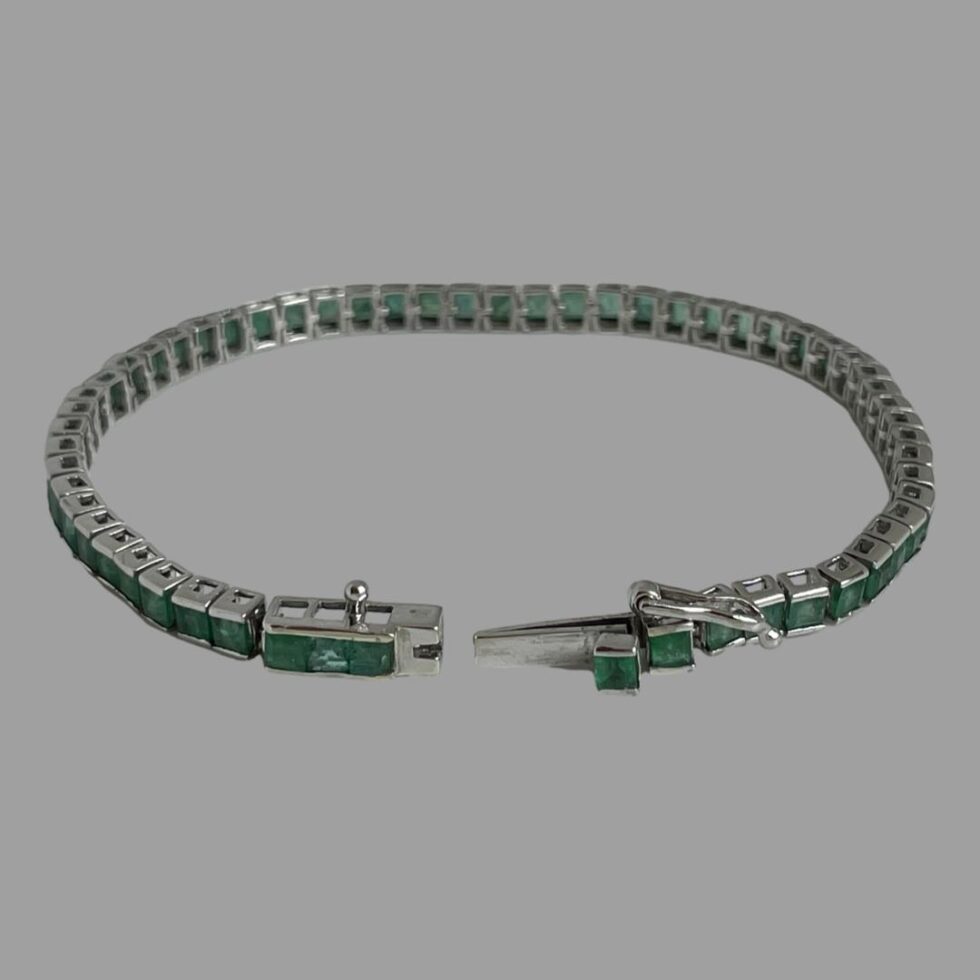 Photo of white gold emerald bracelet displayed in a circle with the clasp in the foreground. The clasp is shown undone and slightly apart.