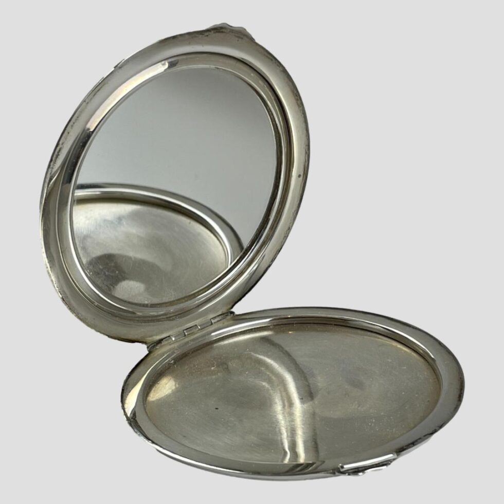 Photo of sterling silver enamel mirror displayed open with and facing to the bottom right corner. The mirror is reflecting part of the base cover of the mirror compact and is in good condition.