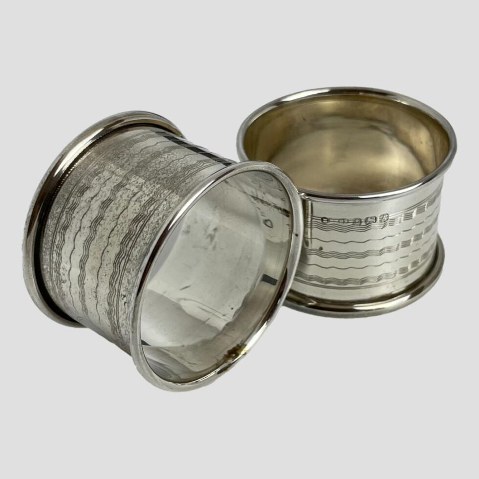 Photo of the 2 rings outside their case with one in foreground on its side and other upright. The hallmark is visible to outside of top rim on upright one.