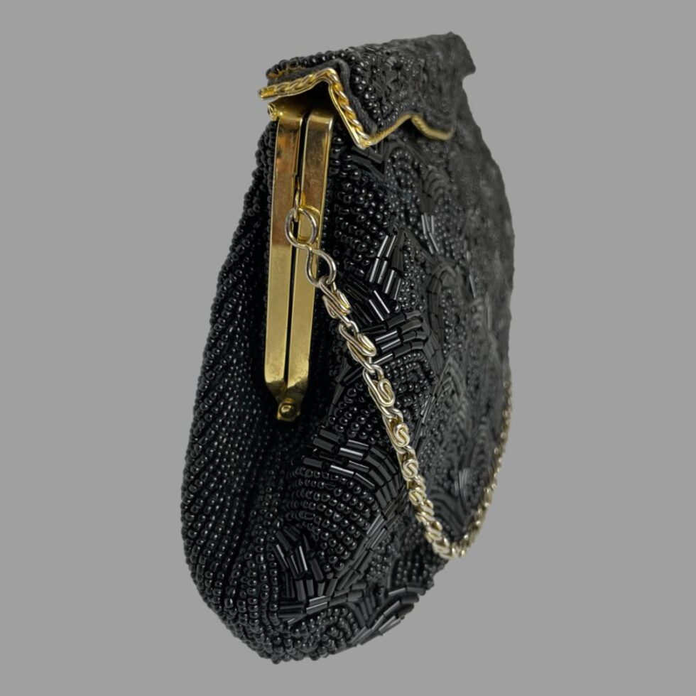 Photo of vintage black beaded bag seen from a side angle with the front facing towards the right.