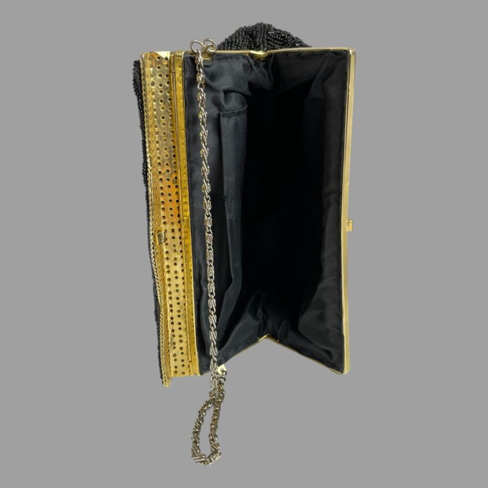 Photo of vintage black bead bag displayed open on its side showing the rigid opening flap. The interior has one pocket to the back.