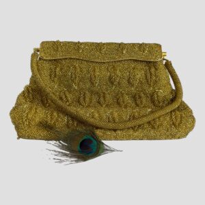 Main photo of vintage gold beaded bag displayed with the front opening side on display. The handle is laid across the front of the bag. A single short peacock feather is in the foreground for display. There is incredible work that has gone into stitching the beads on this bag.