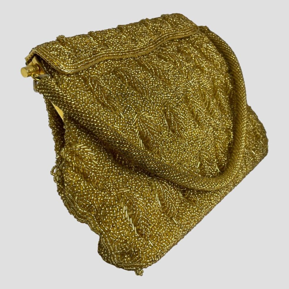Photo of gold beaded bag displayed from a slight side angle with the bag front facing towards the right. The handle is still displayed across the front in a wide U shape.
