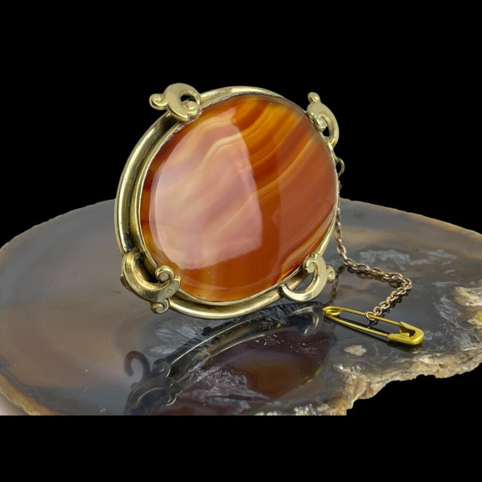 Photo of Victorian banded agate brooch still displayed on a slice of natural agate with the brooch front facing towards the right this time. The studio light is bouncing off the brooch agate on the left.