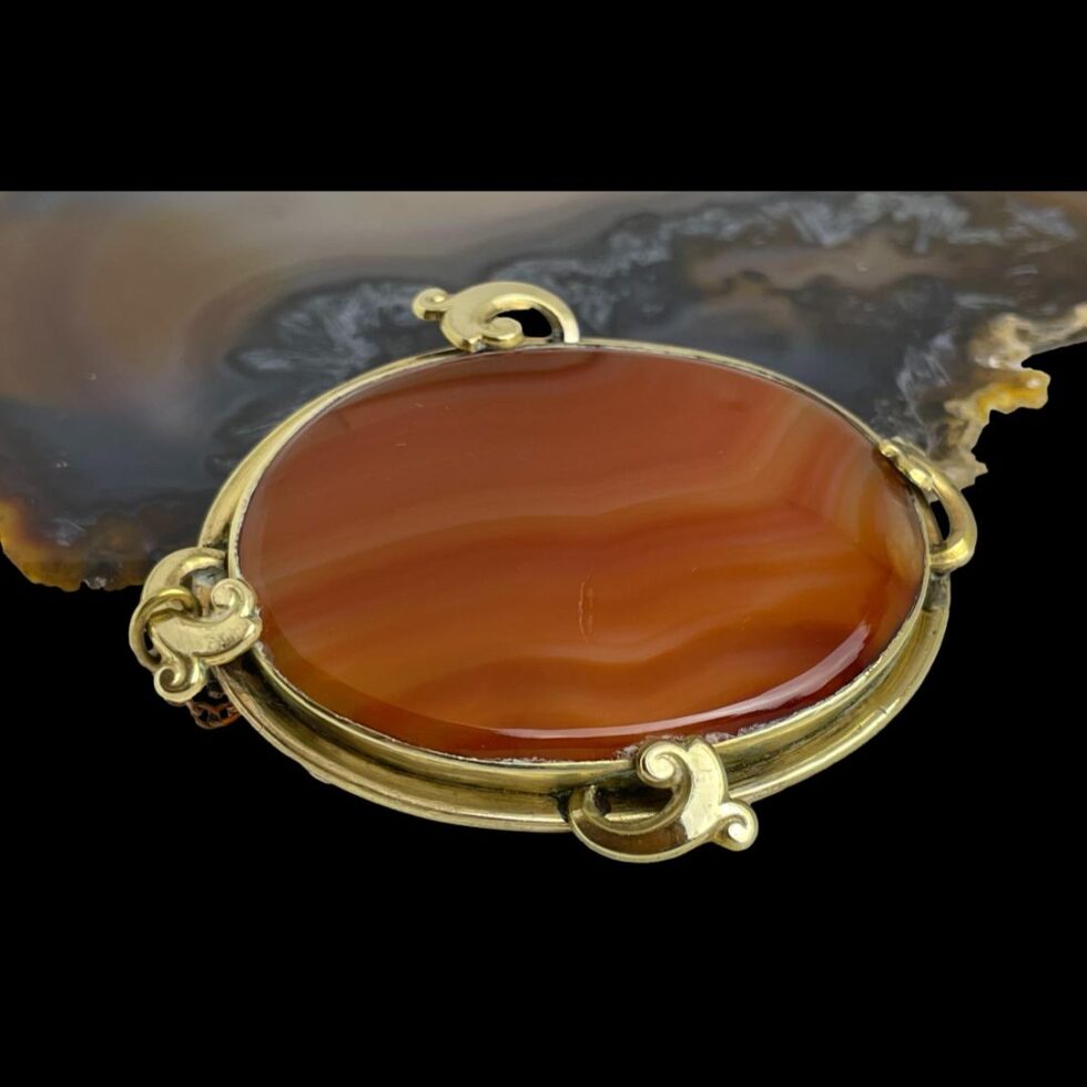Photo of Victorian banded agate brooch displayed leaning almost flat against the slice of natural agate. The brooch front is facing up and slightly to the right.