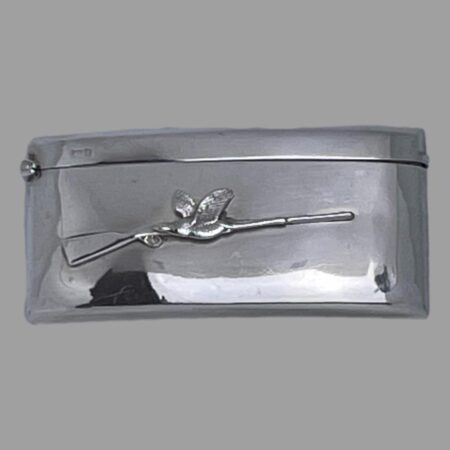 Main photo of antique business card case displayed on a flat surface and looking down at the front of the case. (The studio light and cover is reflecting on case in the shot) The case has a curved design so it will sit snuggly inside a back trouser or breast pocket. Other than the sleek design, the only decoration to this piece is a applied rifle at the centre with the stock end on the left and barrel on the right. In contrast, the single game bird is flying the other way passed the rifle and is situated at the centre of the rifle. This must be the one that got away thank goodness!
