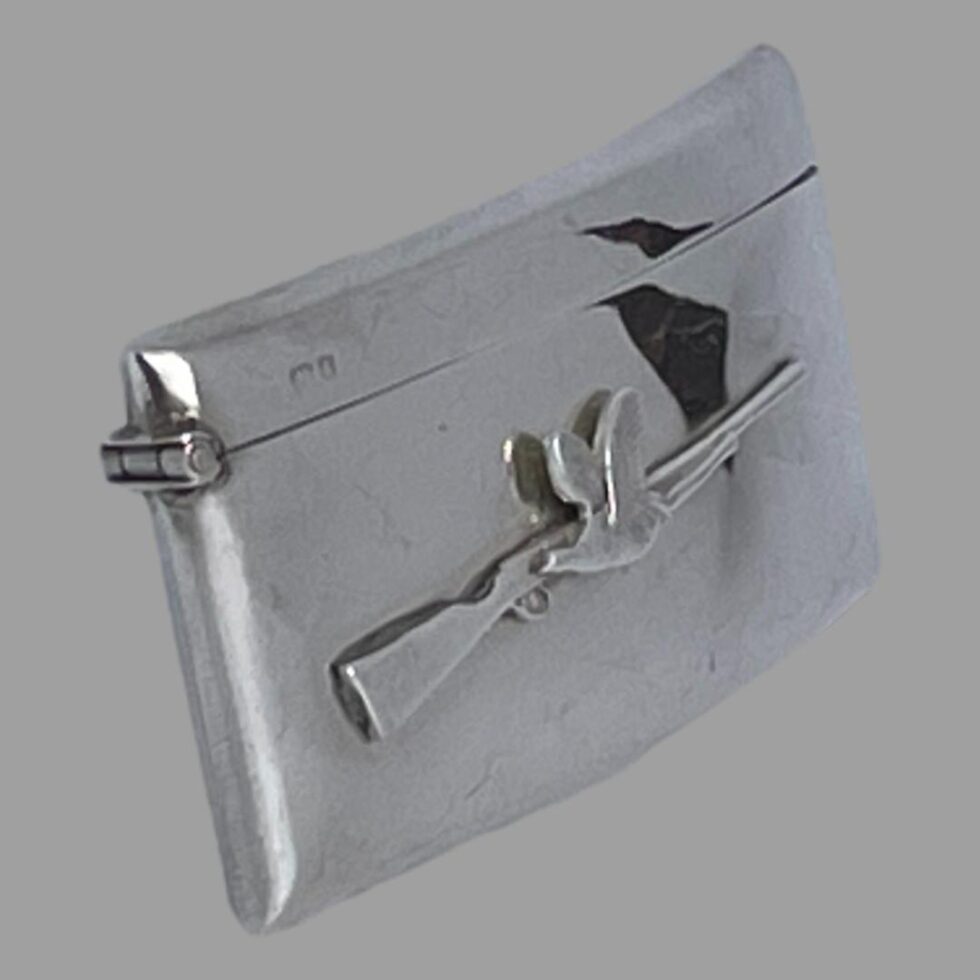 Photo of business card case seen from a slight side angle with the applied decoration side facing towards the bottom right corner of photo. The hinge end is on show as well as the short hallmark at top left corner of case.