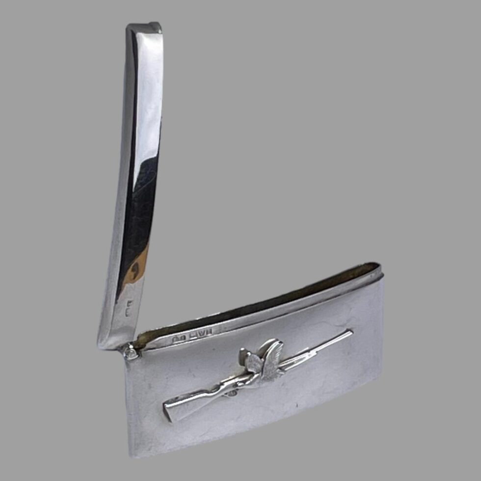 Photo of antique business card case displayed with the top open and stood upright. The rifle and bird side is in the foreground. On the inside rim to the left, the full hallmark is just visible.