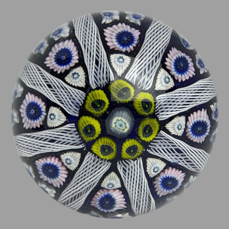 Main photo of Strathearn glass door knob displayed with just the glass area on display (metal fixing bot visible) We are looking straight down at the glass domed knob from above. A single white millefiori with light blue innards takes centre stage framed ed by 7 yellow. From these yellow millefiori, 8 beehive lines divide the dome with each triangle between housing further millefiori pieces in white and pale pink. The base colouring is a lovely cobalt blue which can also be found at the centre of some of the millefiori glass pieces. A stunning art glass door knob for a special door. Great gift!