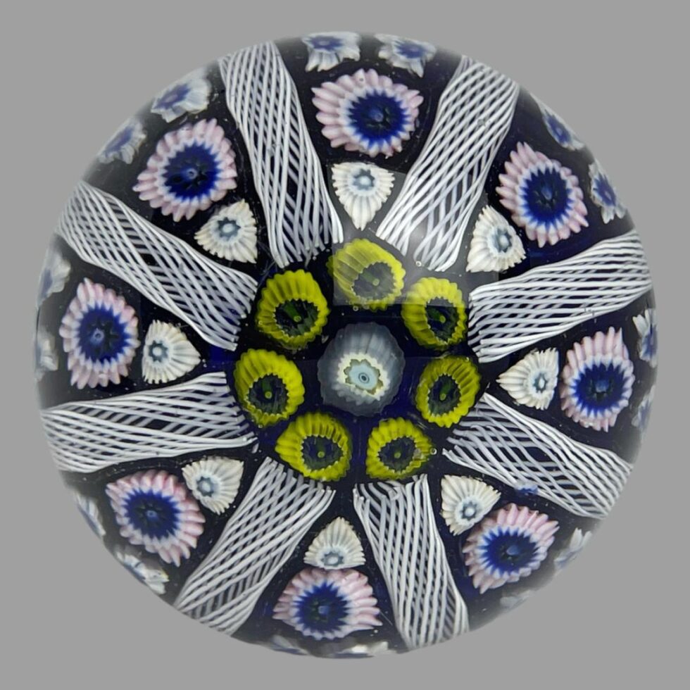 Main photo of Strathearn glass door knob displayed with just the glass area on display (metal fixing bot visible) We are looking straight down at the glass domed knob from above. A single white millefiori with light blue innards takes centre stage framed ed by 7 yellow. From these yellow millefiori, 8 beehive lines divide the dome with each triangle between housing further millefiori pieces in white and pale pink. The base colouring is a lovely cobalt blue which can also be found at the centre of some of the millefiori glass pieces. A stunning art glass door knob for a special door. Great gift!