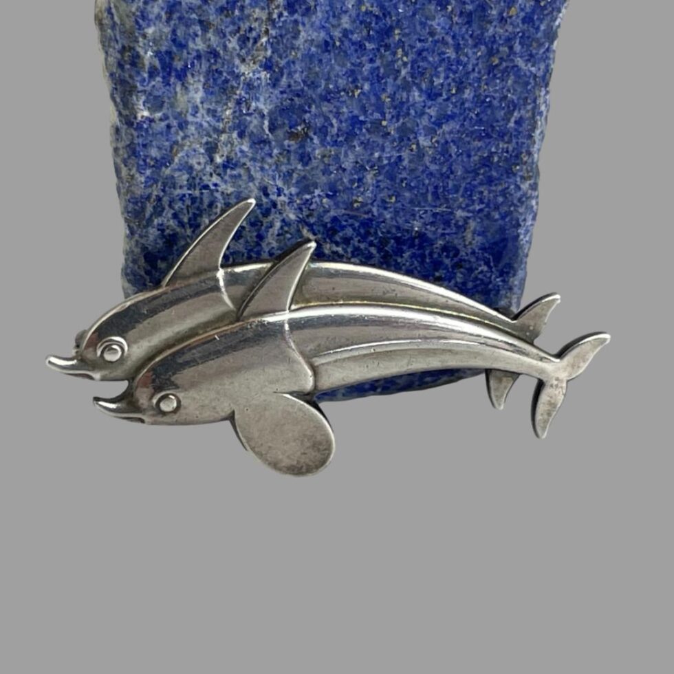 Close up photo of the Georg Jensen dolphins brooch this time leaning against the rock of lapis lazuli. The light is shining better on them here and the simple and elegant detail synonymous with Georg Jensen can be seen.