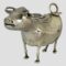 Main photo of Dutch silver cow creamer seen from an eye level with the cows head in the left foreground and curler over tail in the top right corner. The curled tail acts as the handle and the cows mouth is the spout all cleverly concealed! There is a hinged flap on the cows back.