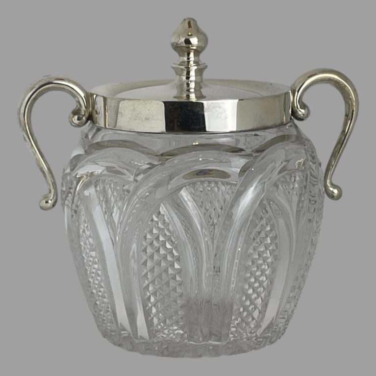 Main photo of glass &silver biscuit barrel seen from an eye level with the handles on left and right. The cut glass base is finely detailed which compliments that plain silver to the top. The silver handles have a upward loop with the ends hanging down to around the most bulbous part of the barrel. They are attached to the silver rim around the mouth. The lid also in silver has a fairly tall finial for easy removal. A lovely piece of late Victorian early Edwardian tableware.