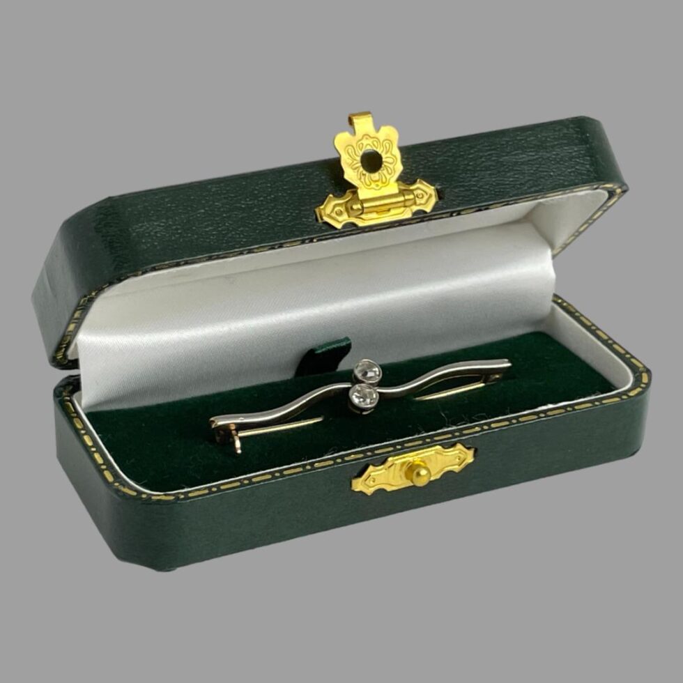 The Edwardian gold diamond brooch still displayed inside its green case this time with the brooch front facing toward the bottom right corner.