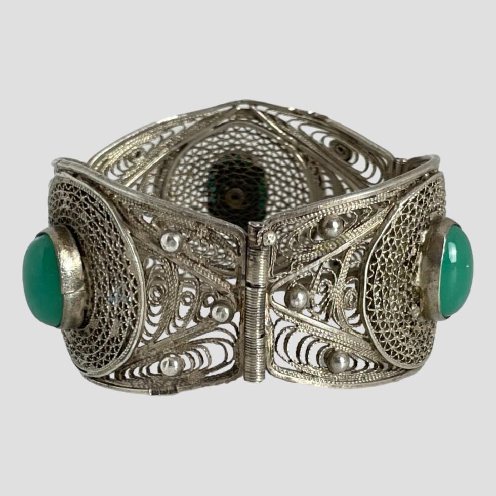 Photo of Egyptian filigree silver bracelet displayed with clasp closed and in the centre foreground. The bracelet is upright with 2 chrysoprase cabochons visible to left and right and the back of third stone is visible behind.