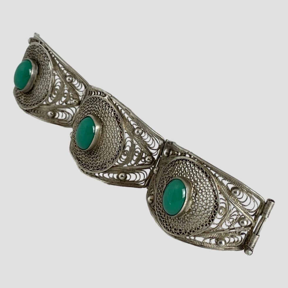 Photo of silver filigree chrysoprase bracelet displayed in a straight line and shown diagonally across the page with one end in top left and other in bottom right corner.