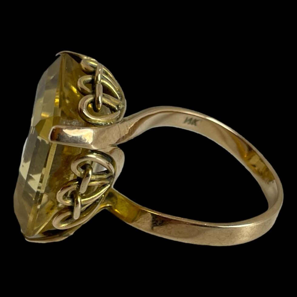 Photo of ring displayed on a flat surface with the ring front facing left. The gold hallmark is just visible to the inside band.