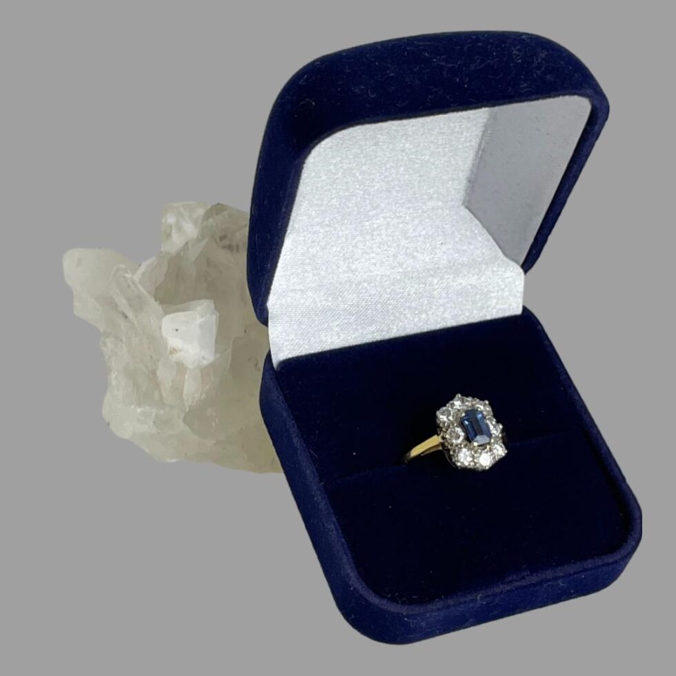 Photo of ring displayed inside a blue velvet box which is propped up against a rock of quartz crystal.