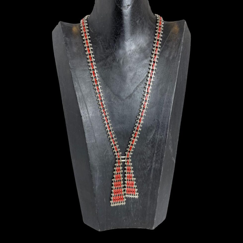 Main photo of Jakob Bengel Mauerwerk necklace displayed on a black wooden display stand and shown. The necklace dates to the Art Deco era and is in chrome and red enamel. Although the necklace gives an impression of a ribbon with loose ends, it is very steampunk in its creation almost like something put together in a garage using nuts and bolts with red enamel embellishment! The design is known as Brickwork.