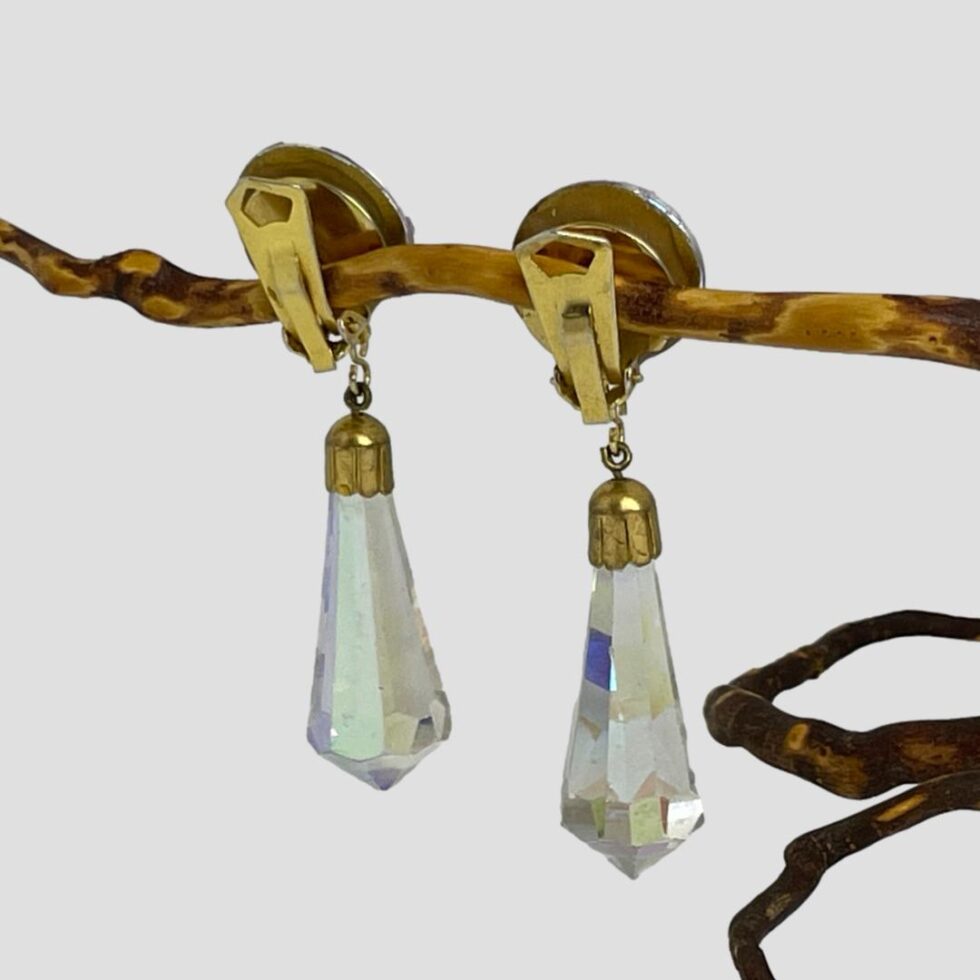 Photo of vintage crystal clip-ons still hanging from a twig and this time seen from the back. Again, the hanging crystals appear clear with a tiny peep of colour within.