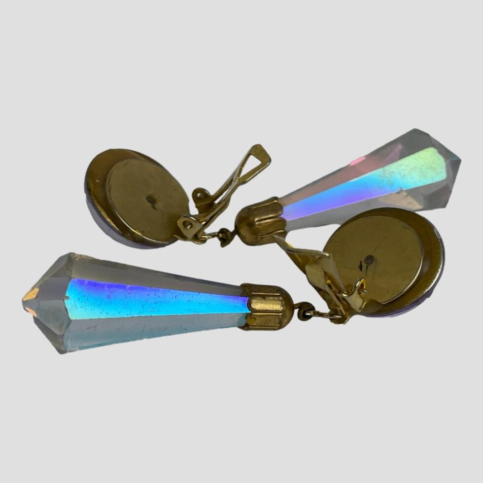 Photo of vintage crystal clip-on earrings laid top to tail on a flat surface with the clips at back shown open on both. The colour of the crystal drops here is incredible! Electric blue, green and purple flashes with hints of pink and yellow.