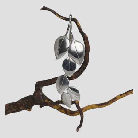 Main photo of silver articulated leaf brooch displayed hanging from a twig of dried cherry tree and looking straight on. The stem end at the top is hooked over a part of twig and the leaves hanging below. The articulated section of the brooch are the 3 leaves at the tip which are securely fastened with bars and loops. Very simple, stylish and elegant brooch.
