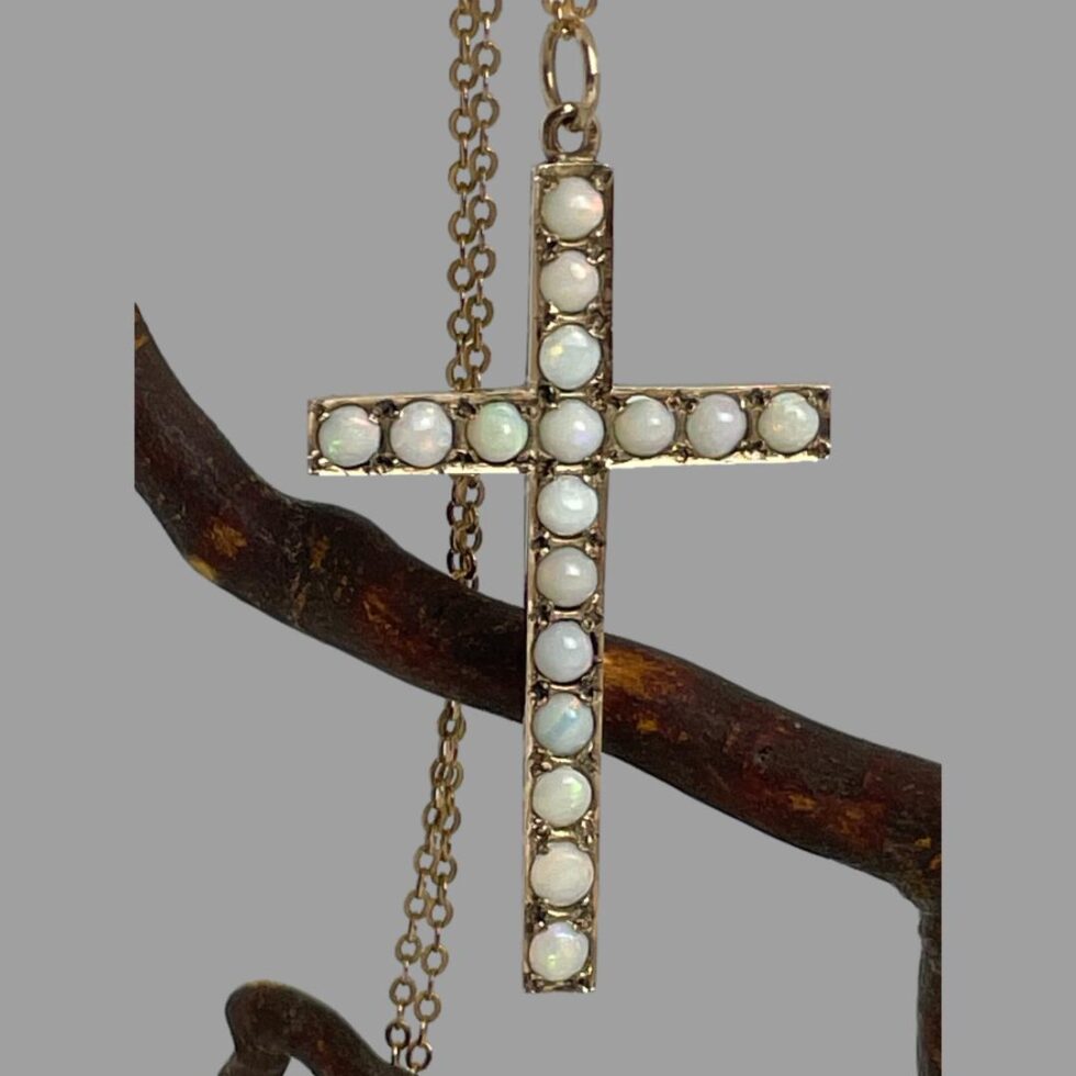 Close up of the gold opal cross shown still hanging from the twig of cherry.