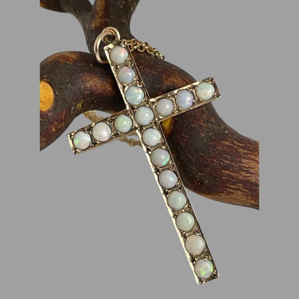 A close up of the front of the cross shown leaning this time against the twig. The colour play in the milky opals is subtle but the pink, green, blue and orange hues are visible.