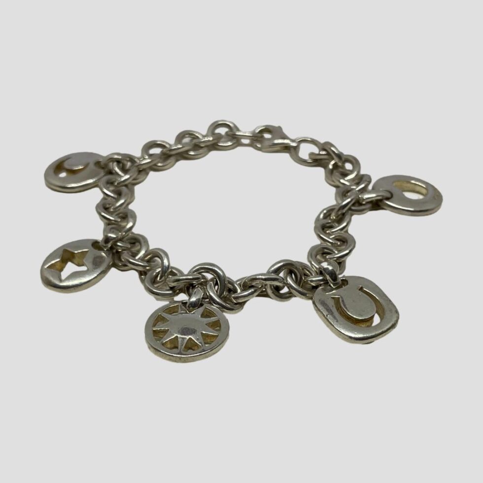 Photo of Tiffany charm bracelet displayed on a flat surface this time with the bracelet clasp closed. The angle is a little lower which shows the silver thickness of the charm pieces.