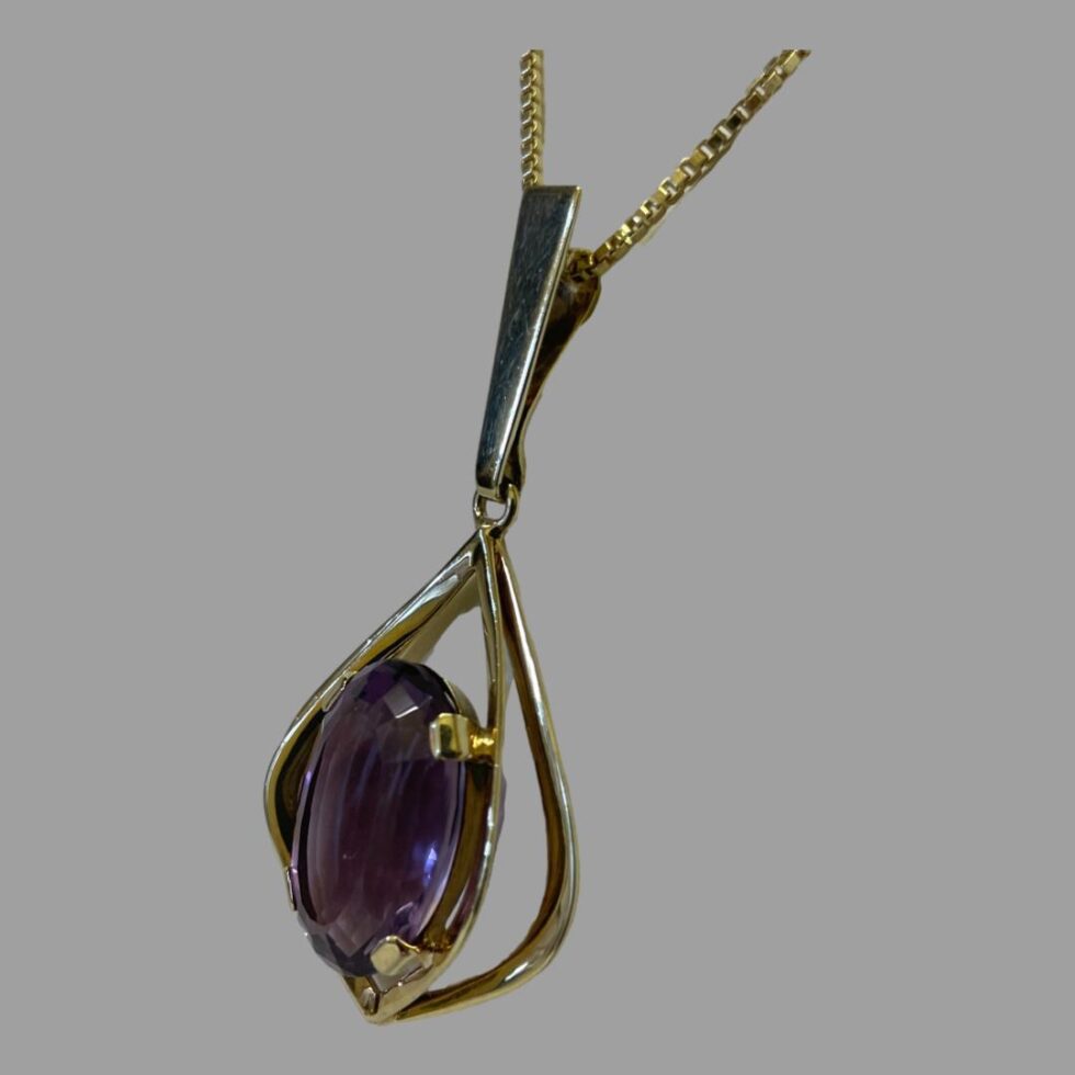 Photo of gold amethyst pendant & chain seen from a slight side angle with the pendant front facing to the left. Here you can see that the actual chain bail sits behind the longer strip at front.